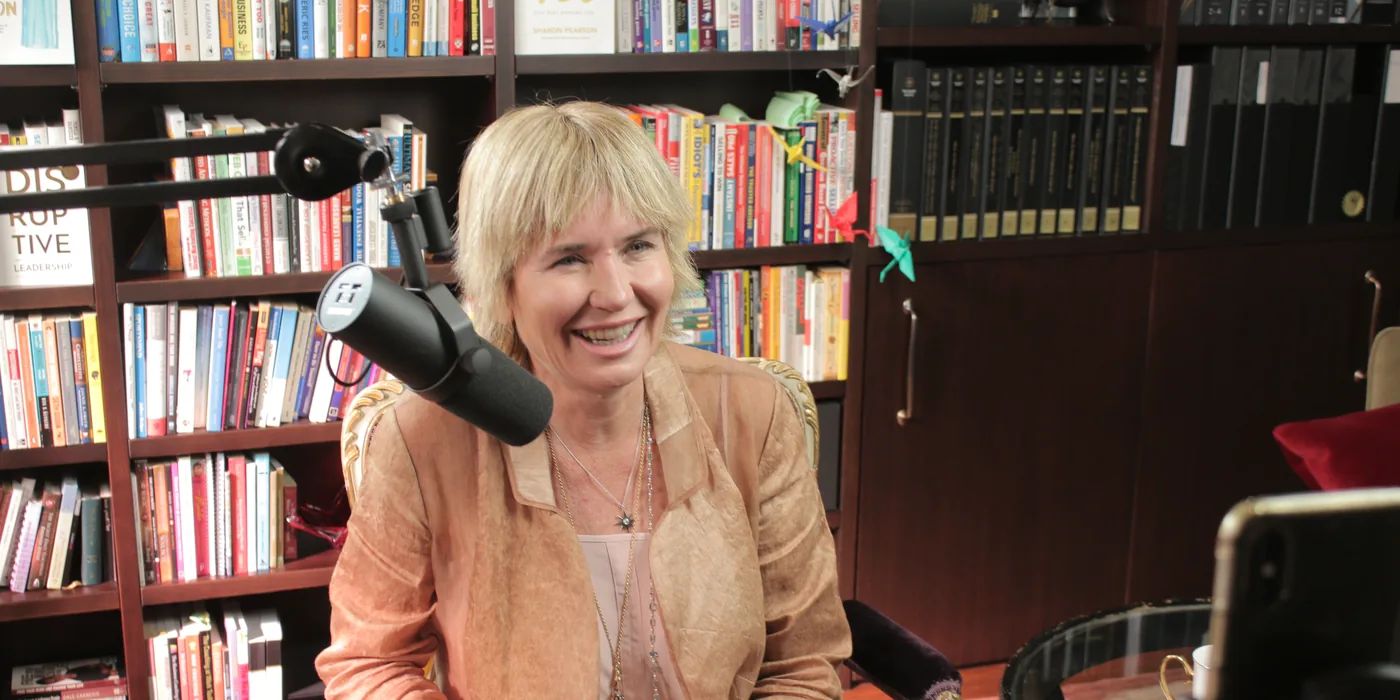 Remi laughing behind a podcast microphone in front of bookshelves