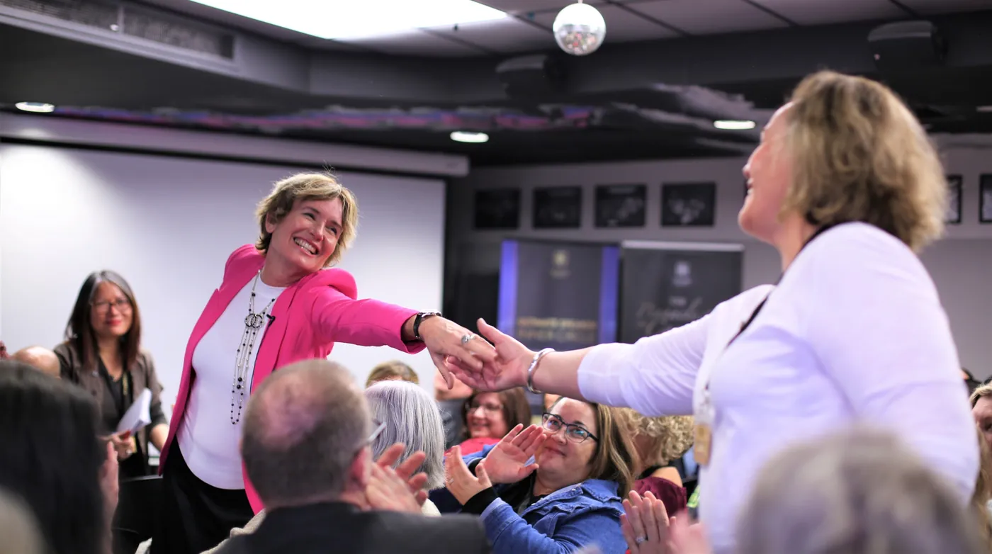 Remi reaching across a crowded room to shake a participant's hand