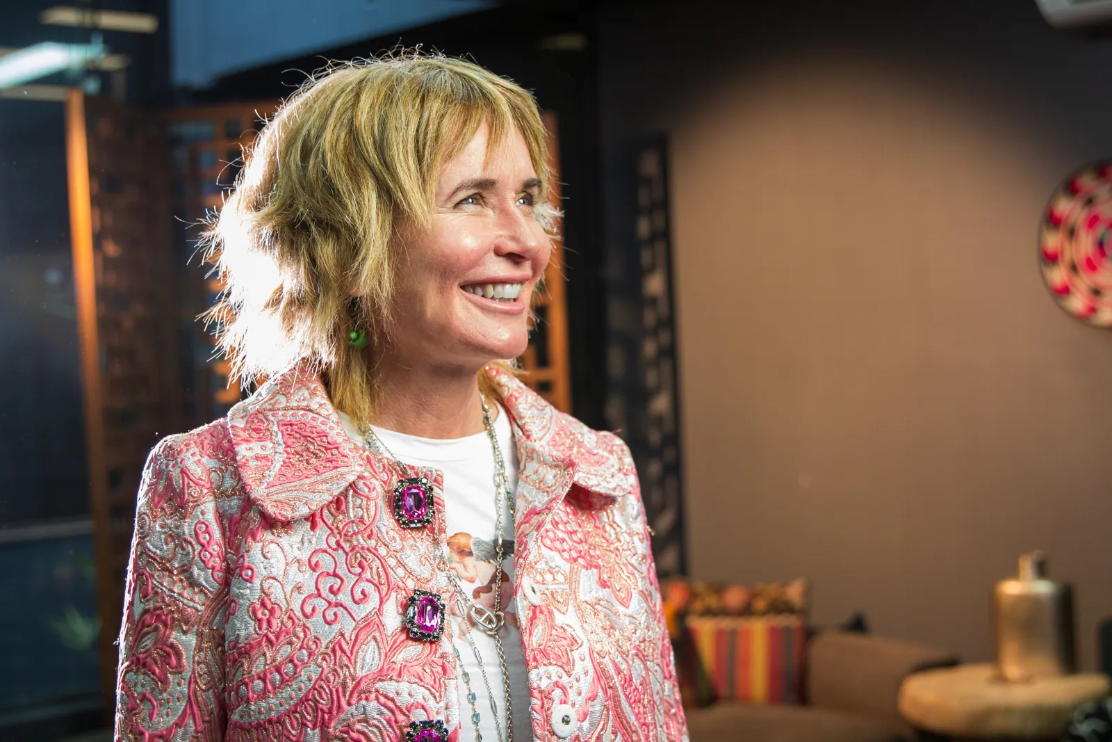 Remi smiling, seated, in a pink patterned jacket