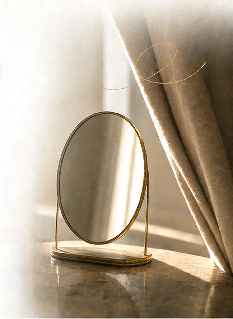 An oval brass mirror on a marble table beside a linen curtain, in late sunlight